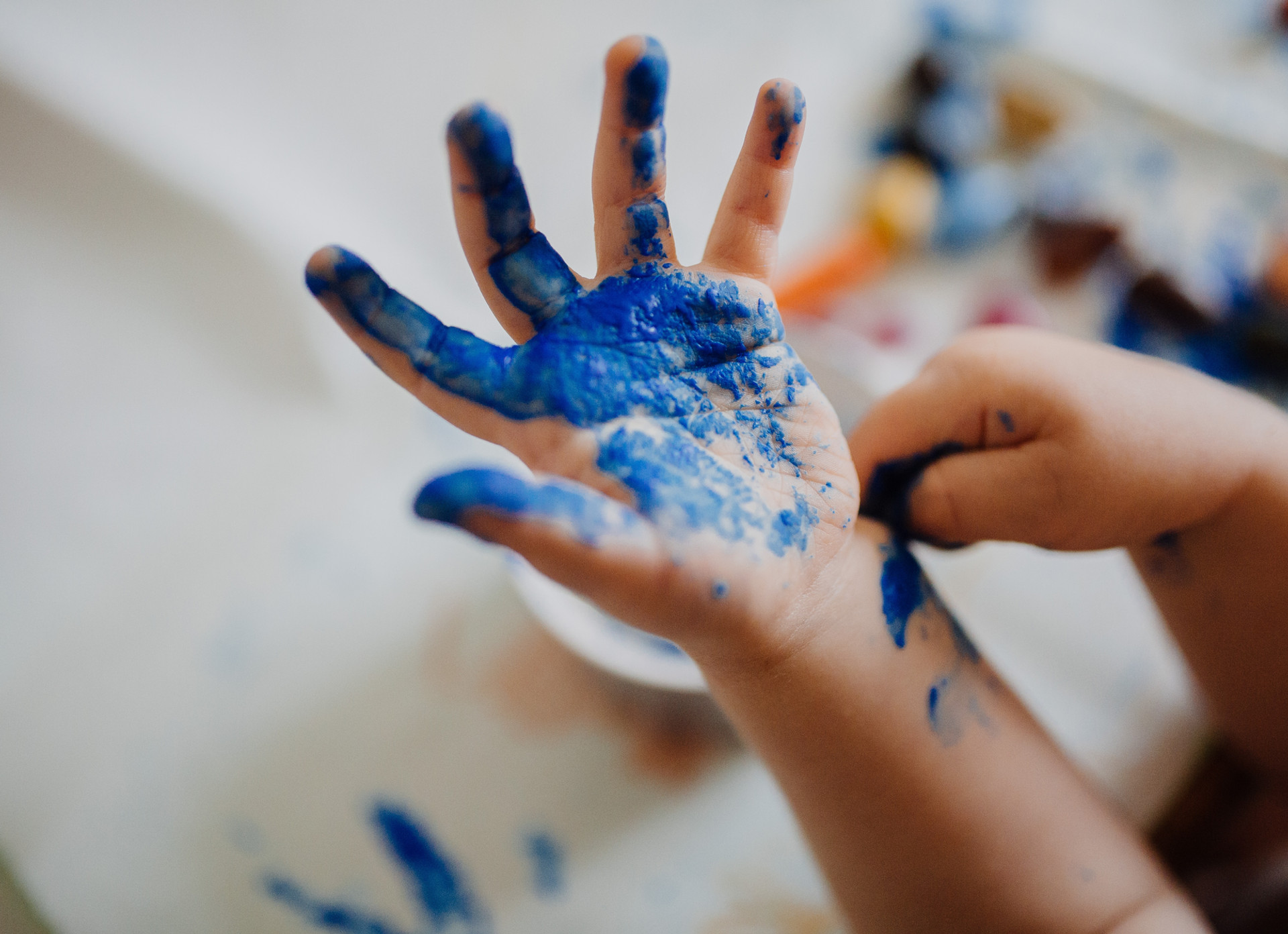 Mãos de criança cobertas de tinta azul durante uma atividade de pintura